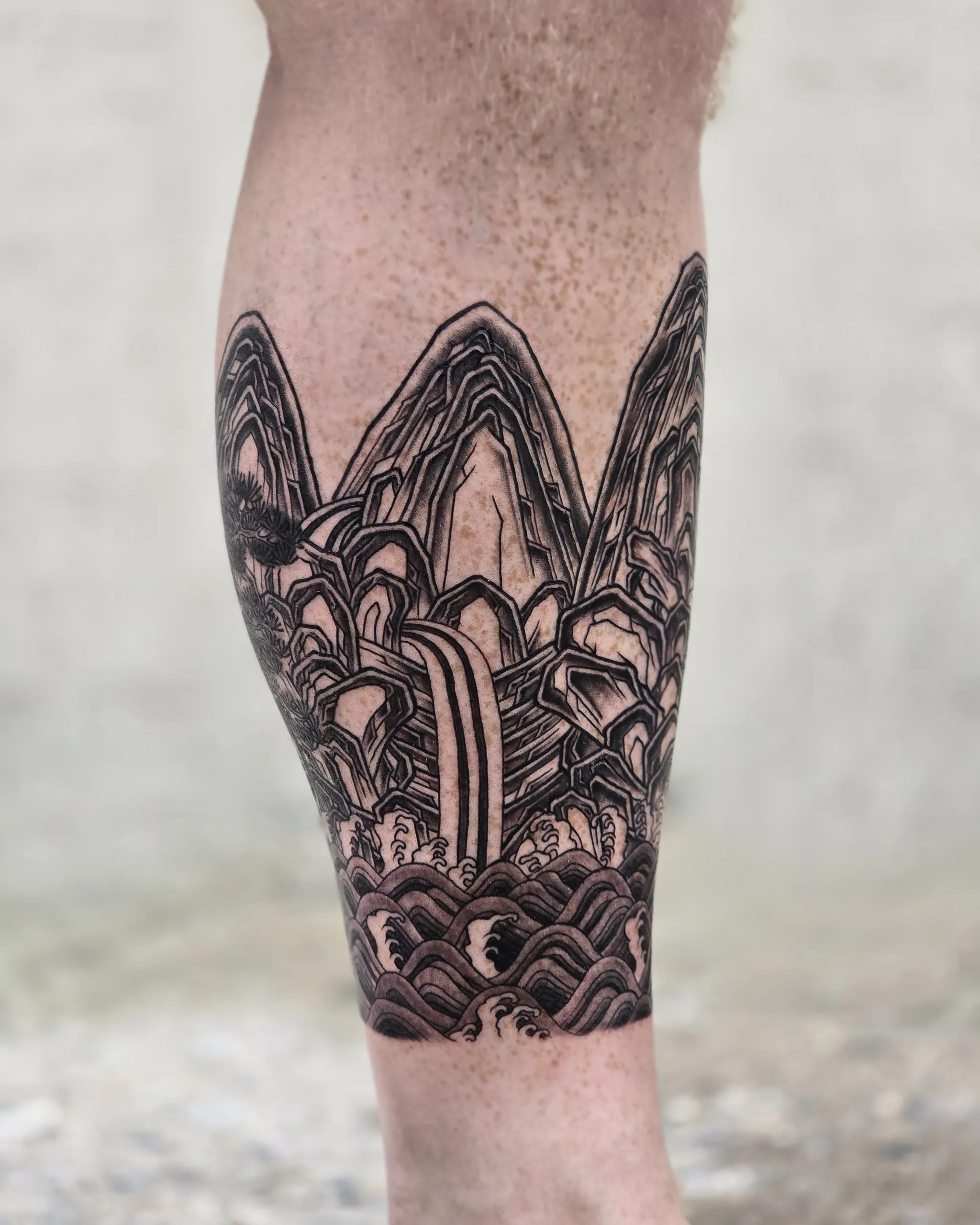 Five Peaks Landscape — a black-and-grey calf tattoo reworking Ilwolobongdo with five peaks, pine trees, waterfalls and waves